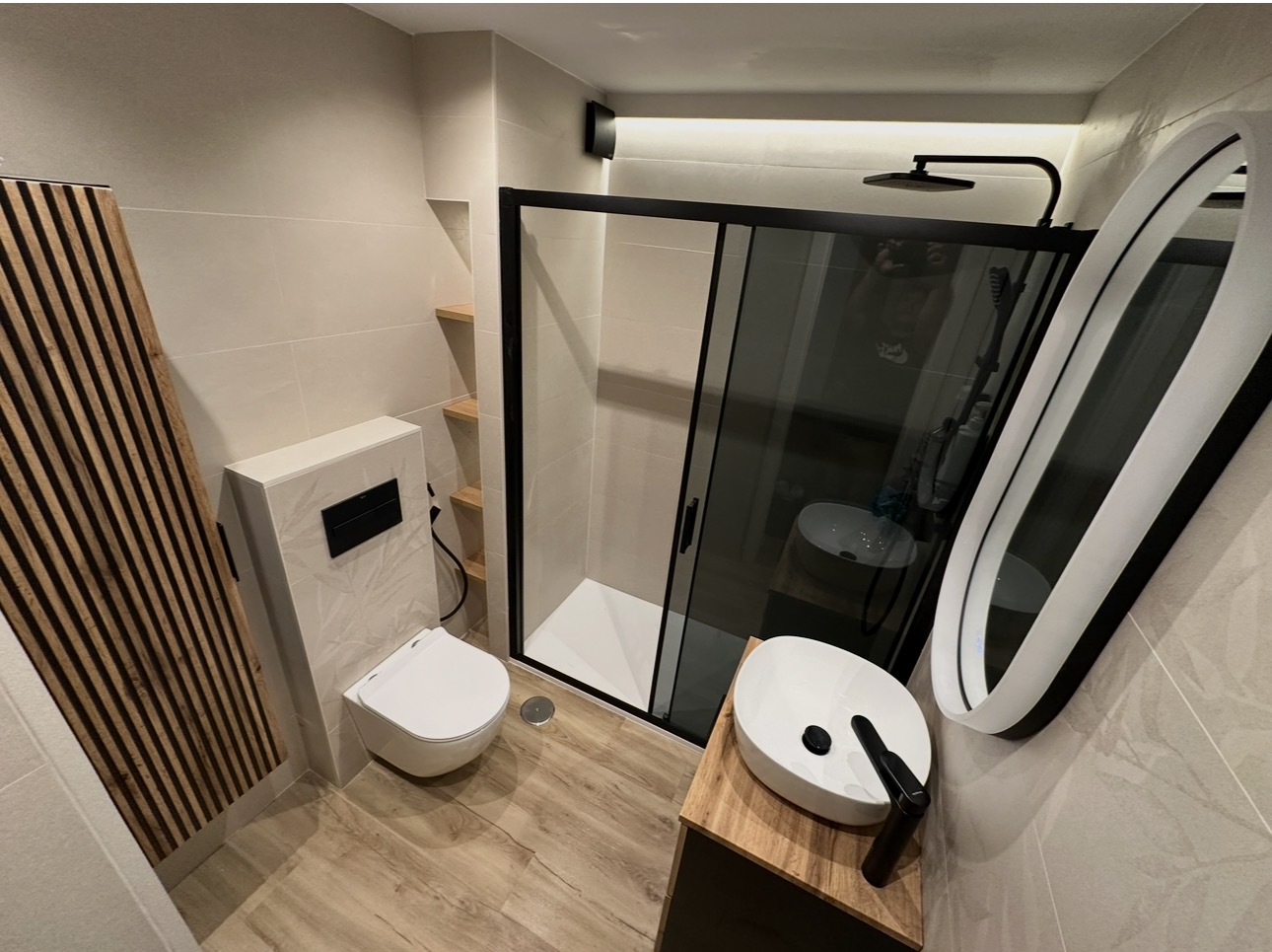 Fotografía real del baño terminado, con ducha, inodoro suspendido y lavabo sobre mueble de madera